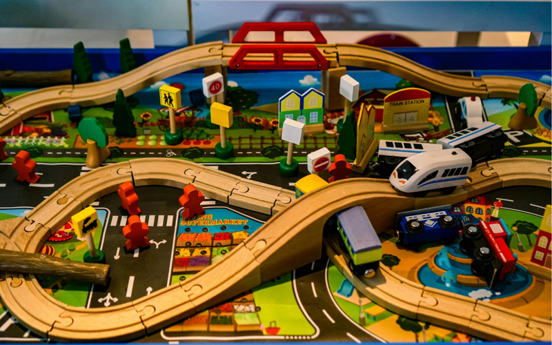 Image shows a toy train track and trains across a model city with roads, houses, shops and people 