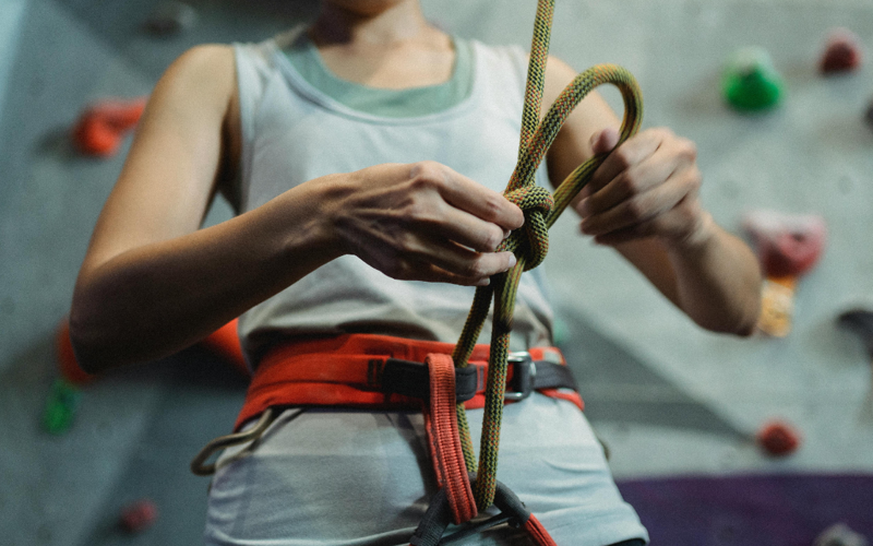 A person knots a safety harness in front of an indoor climbing wall