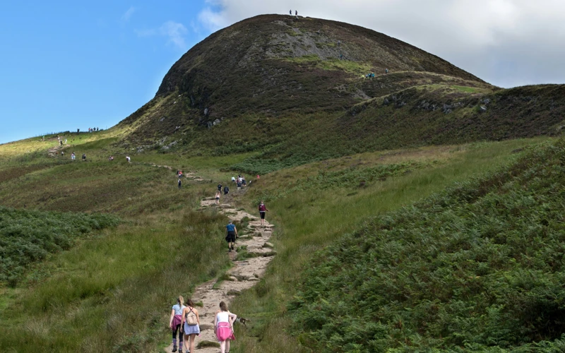 Hillwalkers making their way along a path, with green hill in background