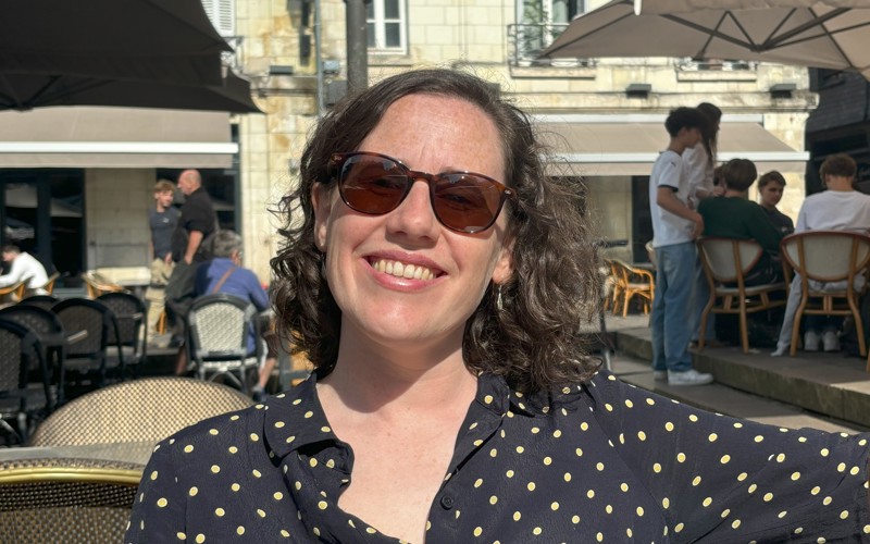 A woman with dark hair and sunglasses smiles to the camera