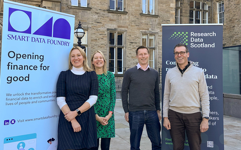 Magdalena Getler, Layla Robinson, Roger Halliday and Dougie Robb stand, smiling, in front of banners for Smart Data Foundry and Research Data Scotland