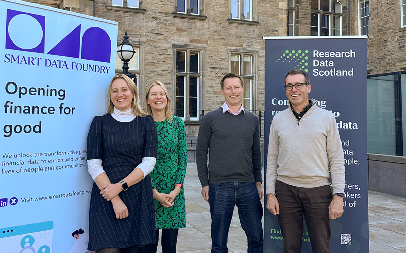 Magdalena Getler, Layla Robinson, Roger Halliday and Dougie Robb stand, smiling, in front of banners for Smart Data Foundry and Research Data Scotland